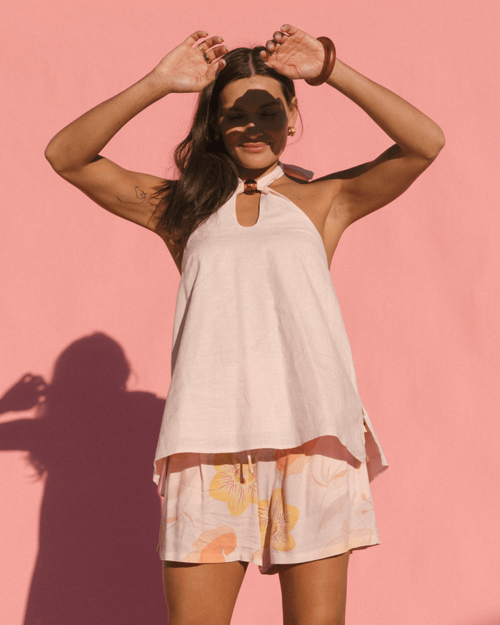 Woman wearing stylish spring outfit with a breathable light pink halter neck top and pink floral floy shorts.