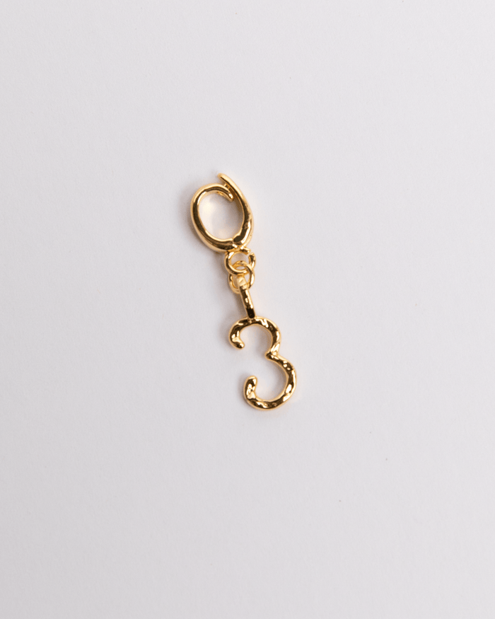A gold-colored charm in the shape of the number 3 with a small loop attachment, displayed against a white background.
