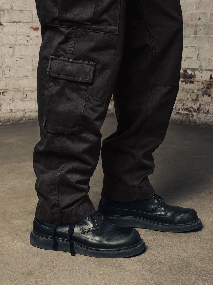 Alpha Industries Acu Pant black cargo pants with utility pockets, paired with black leather shoes.