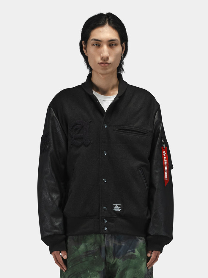 Alpha Industries Alpha Letterman Jacket with black fabric, faux leather sleeves, front pockets, and red sleeve tag.