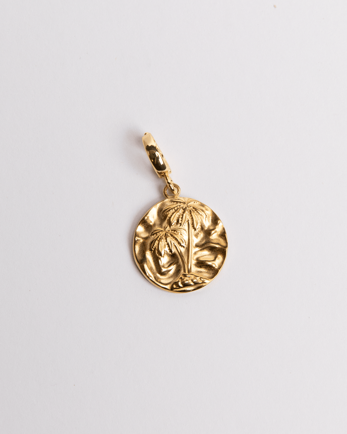 A gold-colored circular charm with a palm design, attached to a small loop for jewelry attachment.
