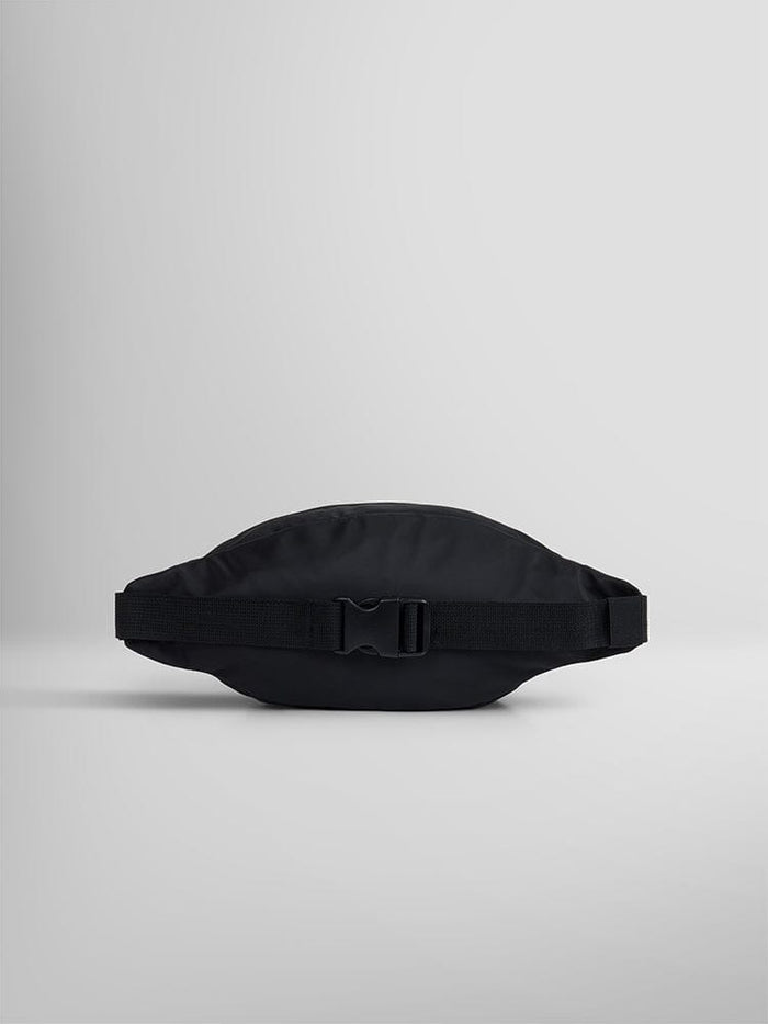 Against a simple gray backdrop, the CREW WAIST BAG by Alpha Industries (FW24-DROP1) stands out with its sleek black design. Made from durable flight nylon, it features a secure buckle and an adjustable waist strap for a comfortable fit on any adventure.