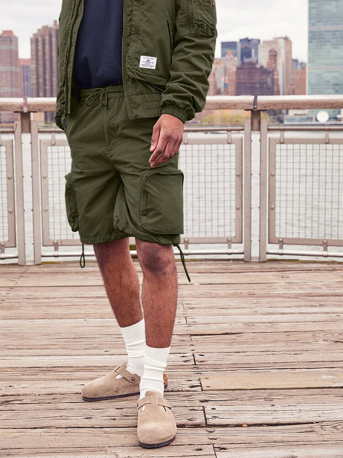 Alpha Industries Cwu 36/P Pull On Short, Olive Green Jacket, White Socks, Tan Slip-On Shoes.