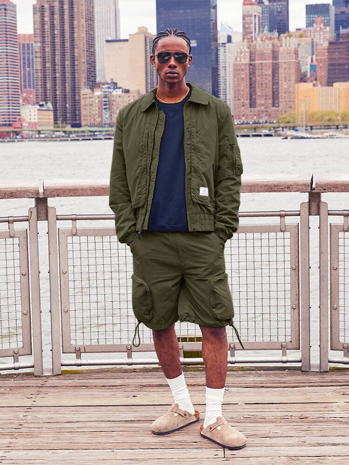 Alpha Industries Cwu 36/P Pull On Short, dark green jacket, black shirt, white socks, brown slip-on shoes.