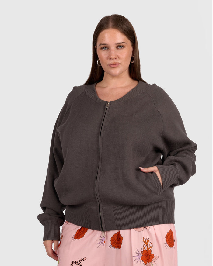 Woman wearing grey zip up jacket with pockets and pink pants.