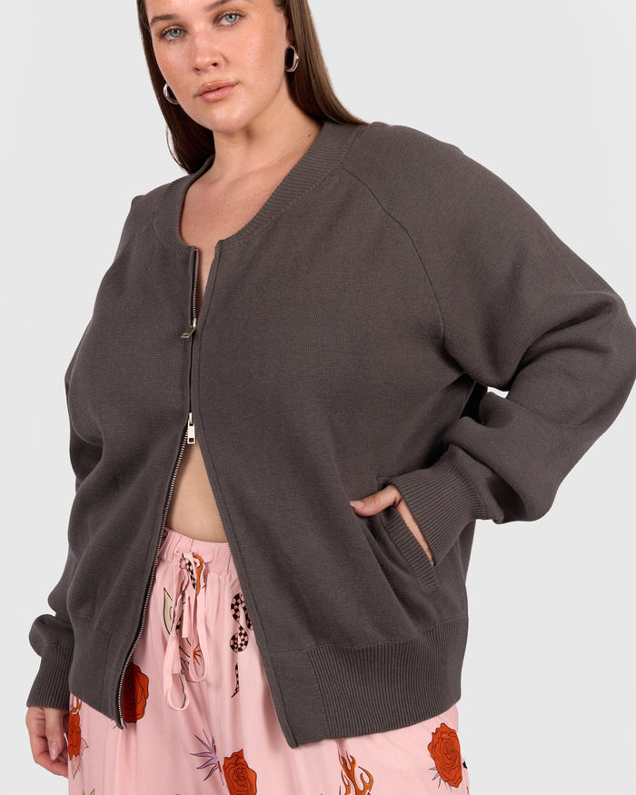 Woman wearing a dark gray cardigan over a pink floral pants on a white background