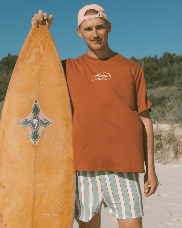 Man wearing rust pj shirt with prawn logo on front and matching striped pj boxer shorts.