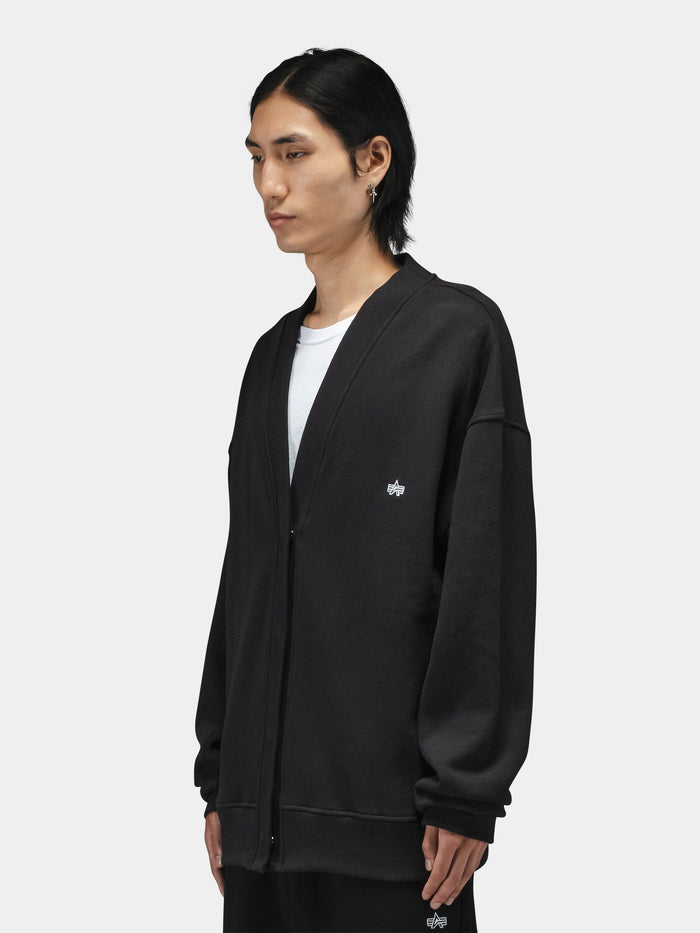 Alpha Industries Essential Cardigan, cotton-poly blend, loose fit, worn over a white shirt.