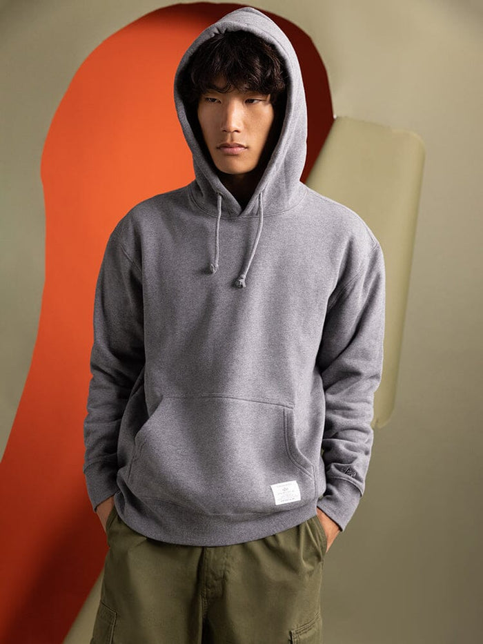 Clad in an Essential Hoodie from Alpha Industries, a person stands with hands in pockets.