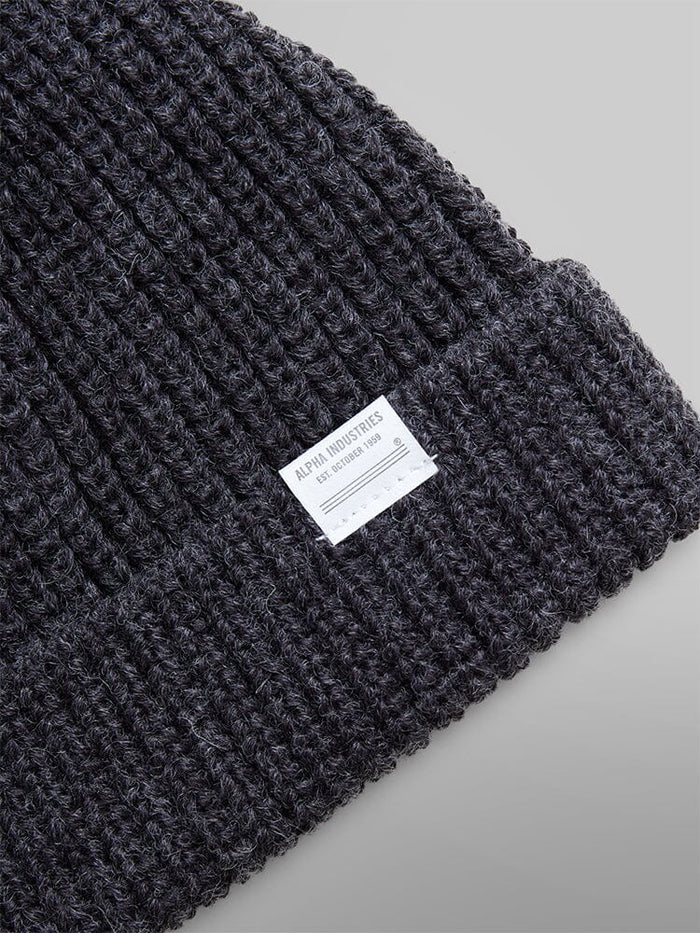 A close-up of the Essential Watch Cap by Alpha Industries in a gray wool-blend, featuring a white label with text, reminiscent of the classic style.