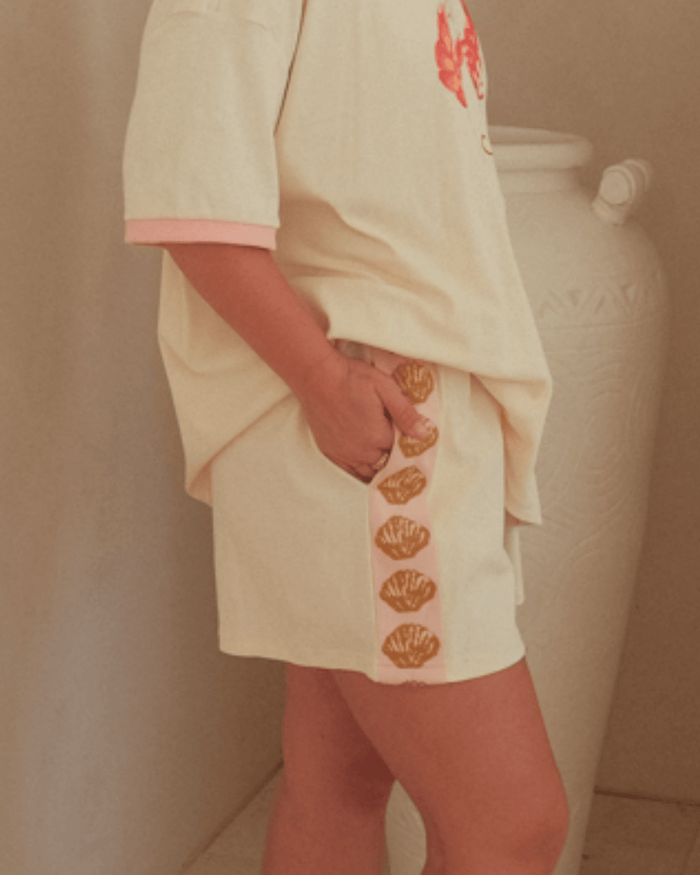 Person wearing a cream-colored matching outfit with gold shell detail on shorts.