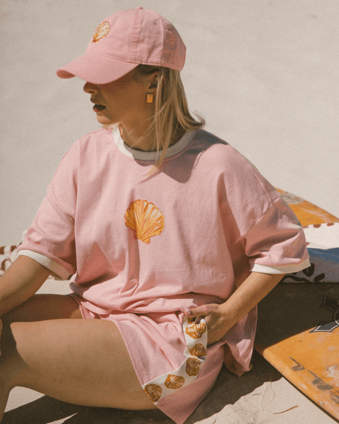 Woman wearing light pink matching outfit with gold shell detailing. The oversized drop-shoulder t-shirt and comfortable high-waisted shorts.