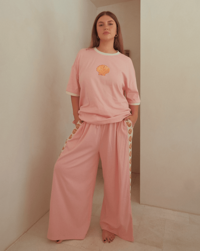 Woman wearing a light pink matching loungewear set with a oversized shirt and wide legged pants.