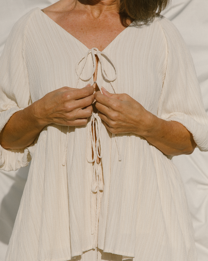 Close-up of woman using modesty clip on breastfeeding friendly cream maternity top.