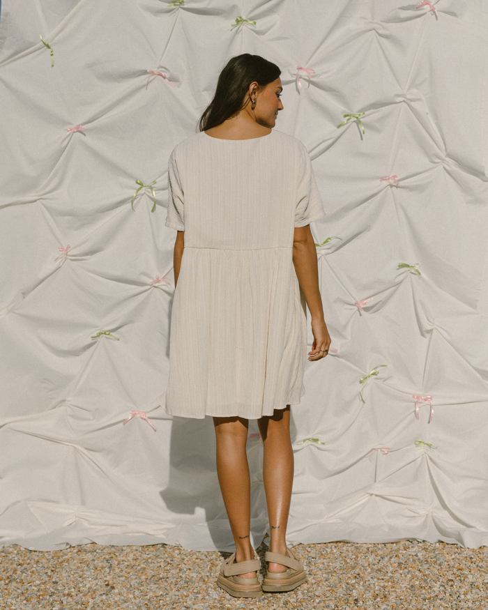Woman wearing a light coloured smock style mini dress in a plisse fabric.