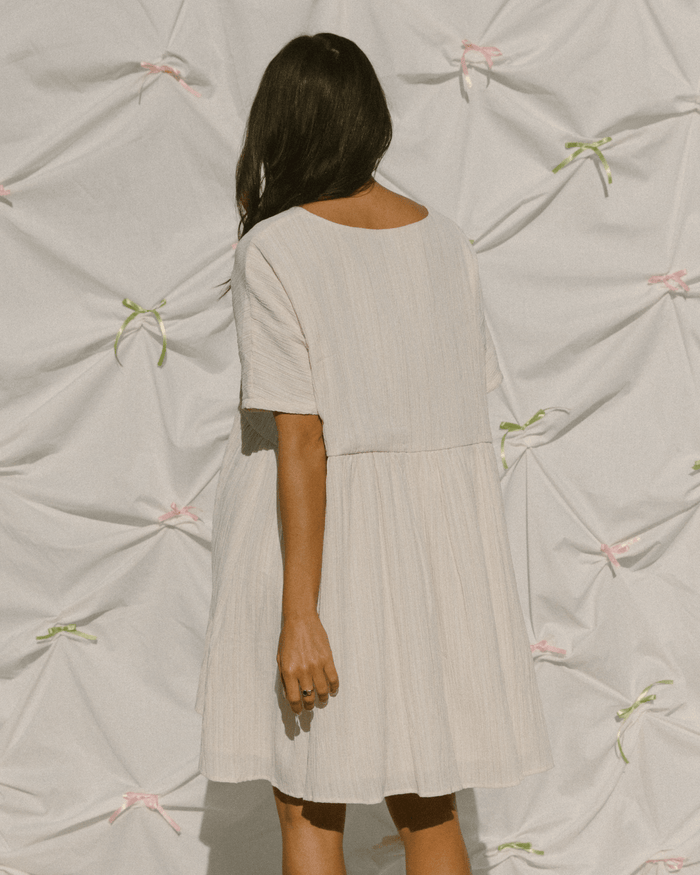 Woman wearing a cream mini dress in plisse crepe fabric.