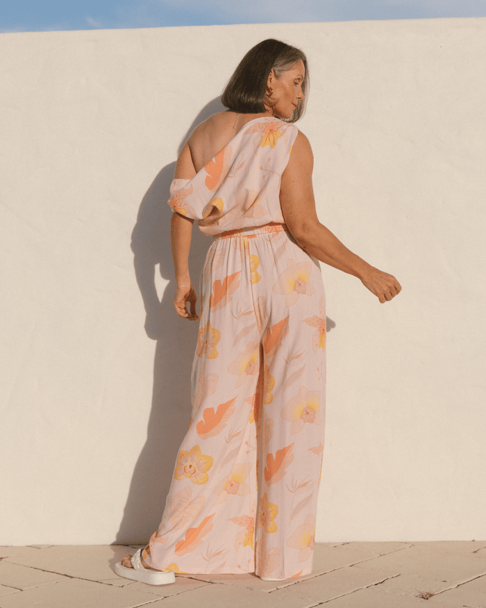 Woman showing back of spring outfit, showing off the shoulder crop top & matching long pants in a pink floral pattern.