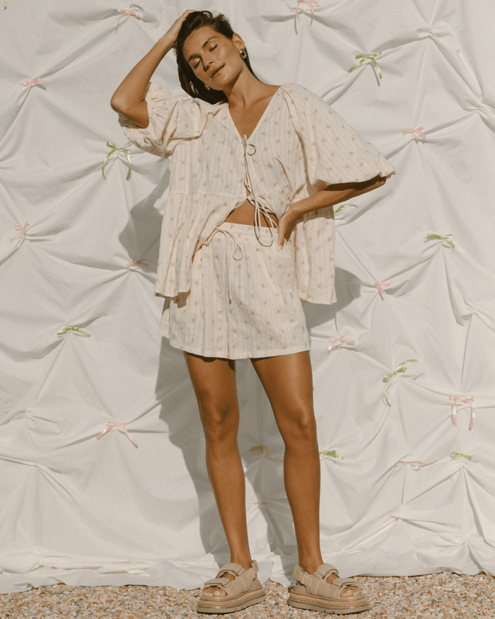 Woman wearing oversized and flowy cream top & shorts set with delicate pink flowers.