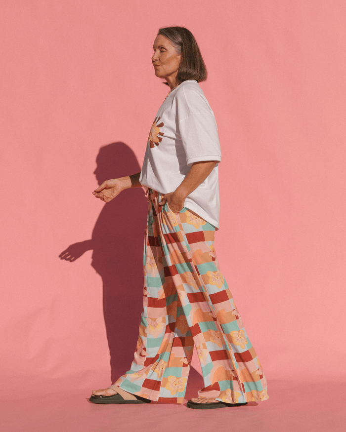 Person wearing a light-colored t-shirt and patterned pants on a pink background