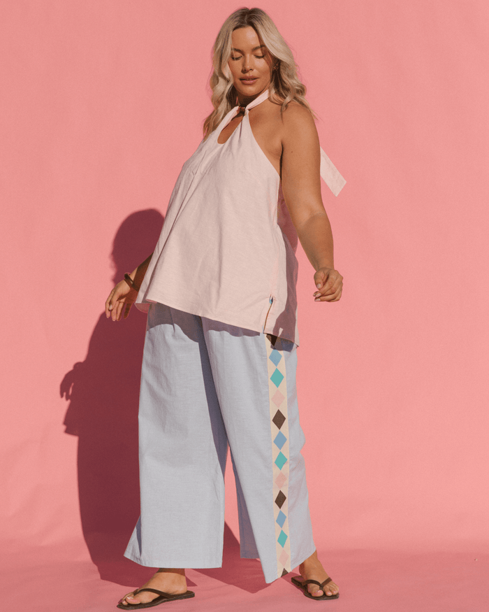 Woman wearing a light pink top and light blue pants with geometric patterns on a pink background