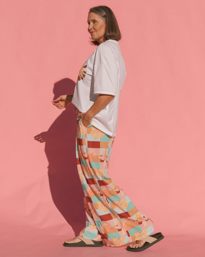 Person wearing a white t-shirt and colorful checkered pants against a pink background