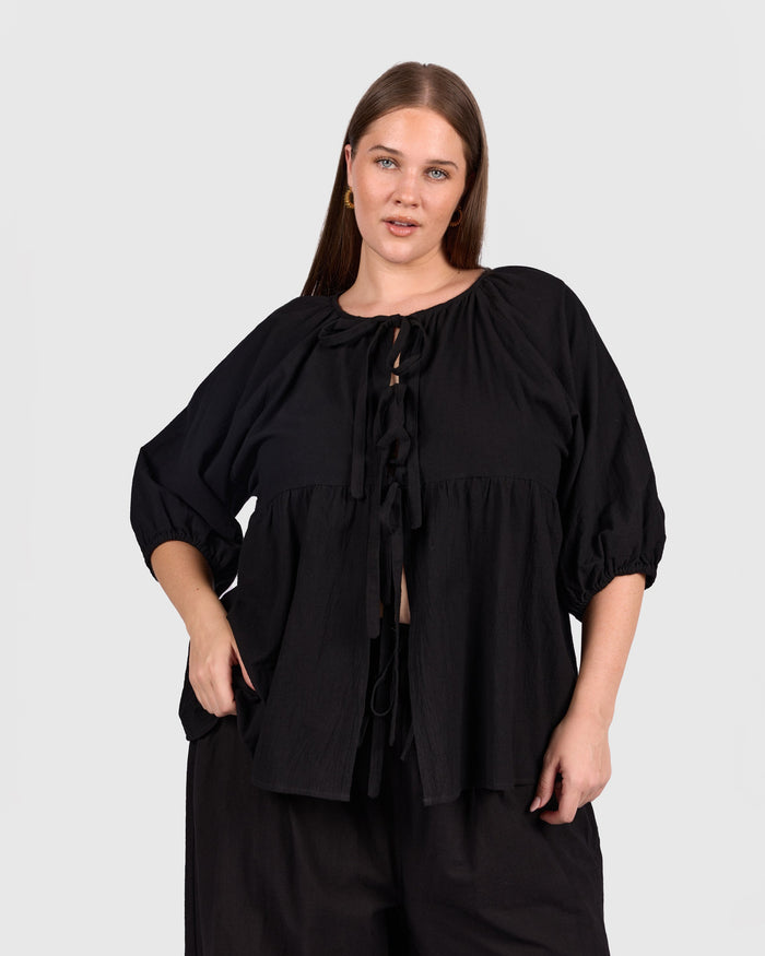 Woman wearing black tie up peplem style shirt.