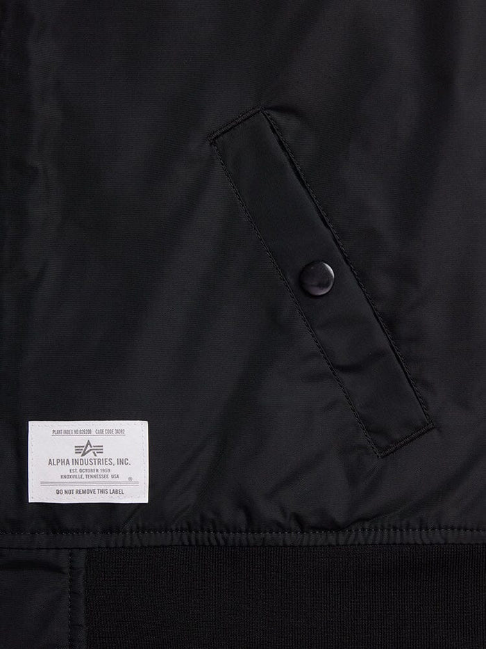 Close-up of a black fabric with a buttoned pocket and a white label reading Alpha Industries, Inc. The L-2B Skymaster Gen II Bomber Jacket W is made from lightweight nylon, offering water-resistant properties and featuring intricate oxygen tab details for enhanced functionality.