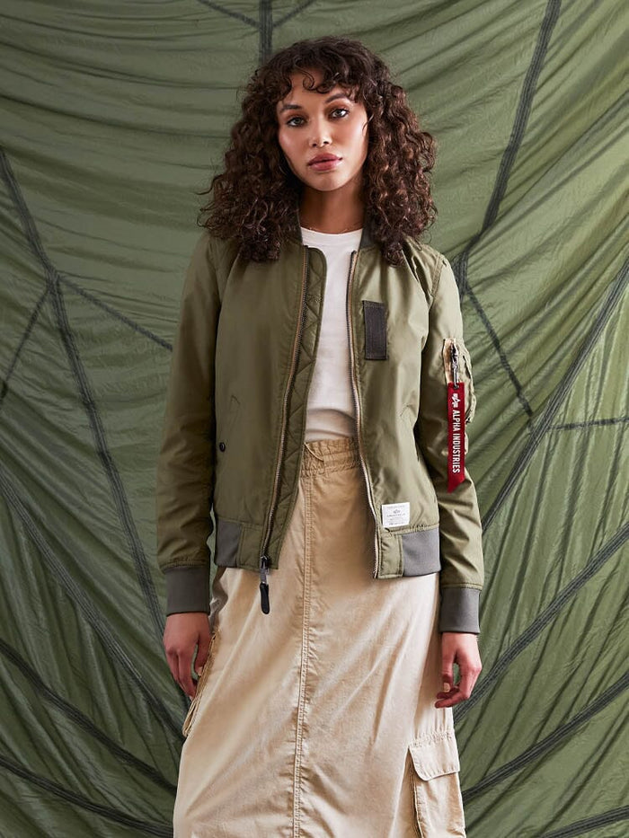 A person wearing the L-2B Skymaster Gen II Bomber Jacket by Alpha Industries, Inc. and a beige skirt stands.