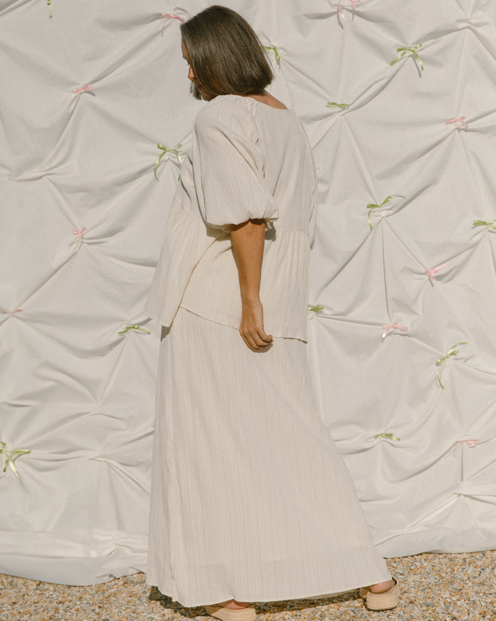 Woman wearing a cream coloured shirt with billowing sleeves and long length skirt.
