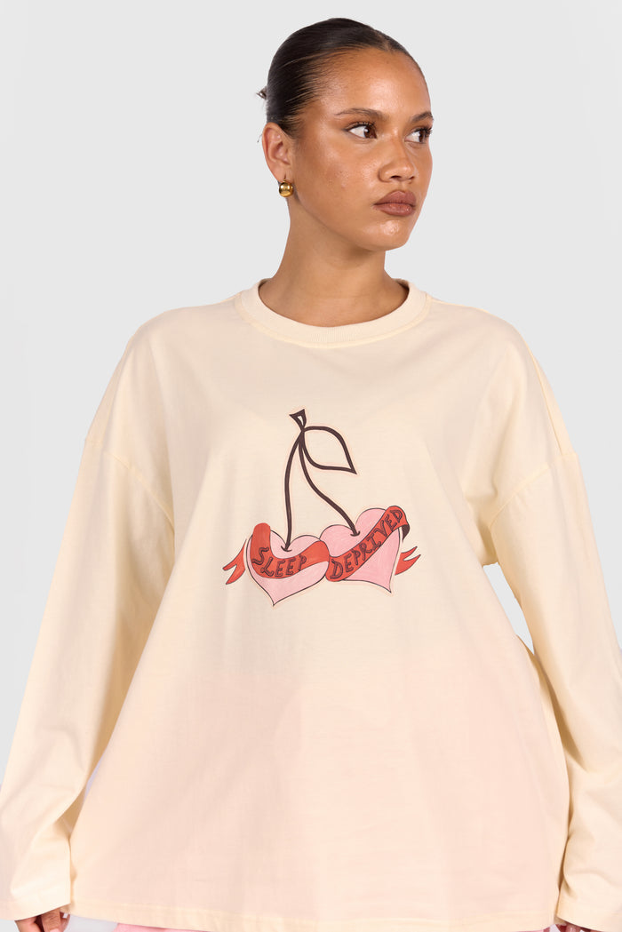 Woman wearing a beige sweatshirt with a cherry design on a plain background