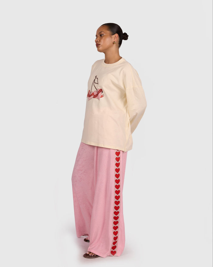 Person wearing a cream sweatshirt with a design and pink pants with heart patterns on a white background