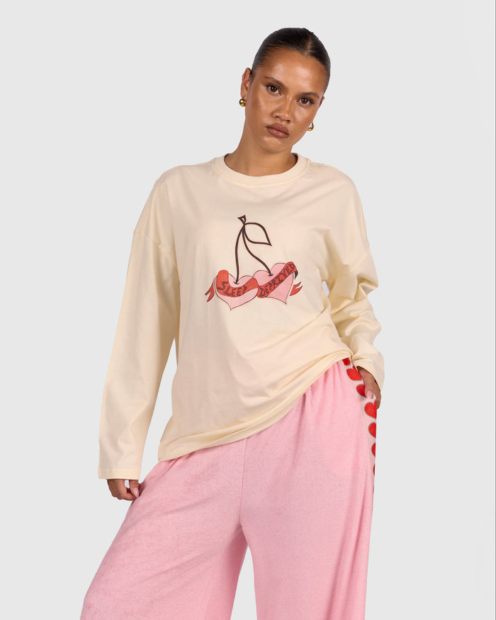 Woman wearing a cream sweatshirt with cherry design and pink pants on a white background