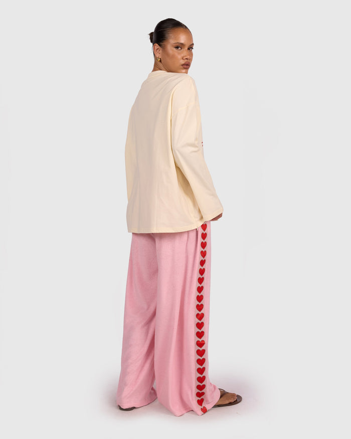 Woman wearing a cream jacket and pink pants with heart details on a white background