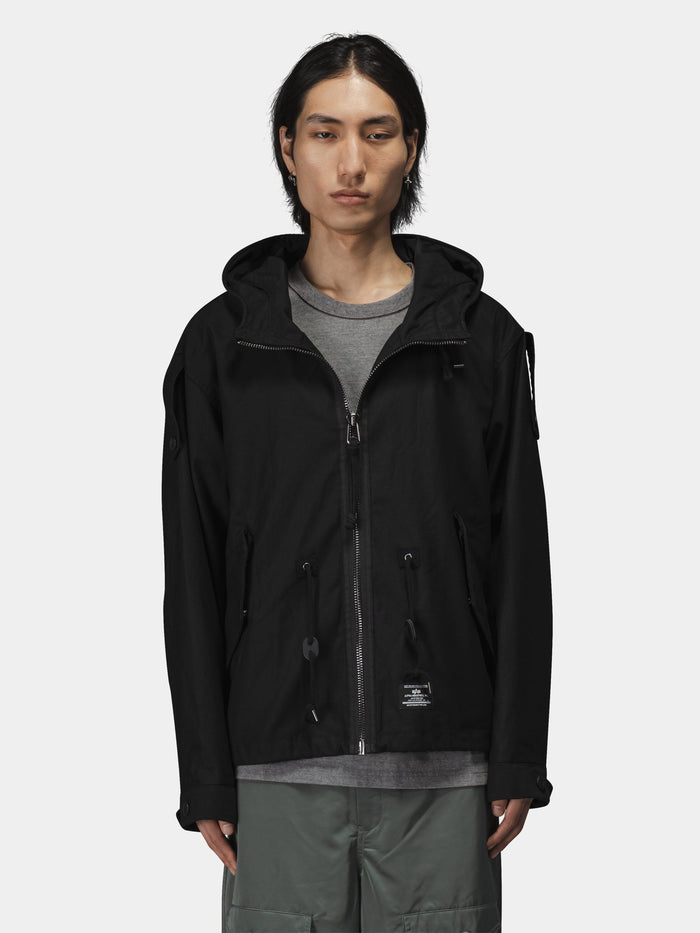 Alpha Industries M-65 Mod Fishtail Field Coat in dark material with fishtail hem over gray shirt and green pants.