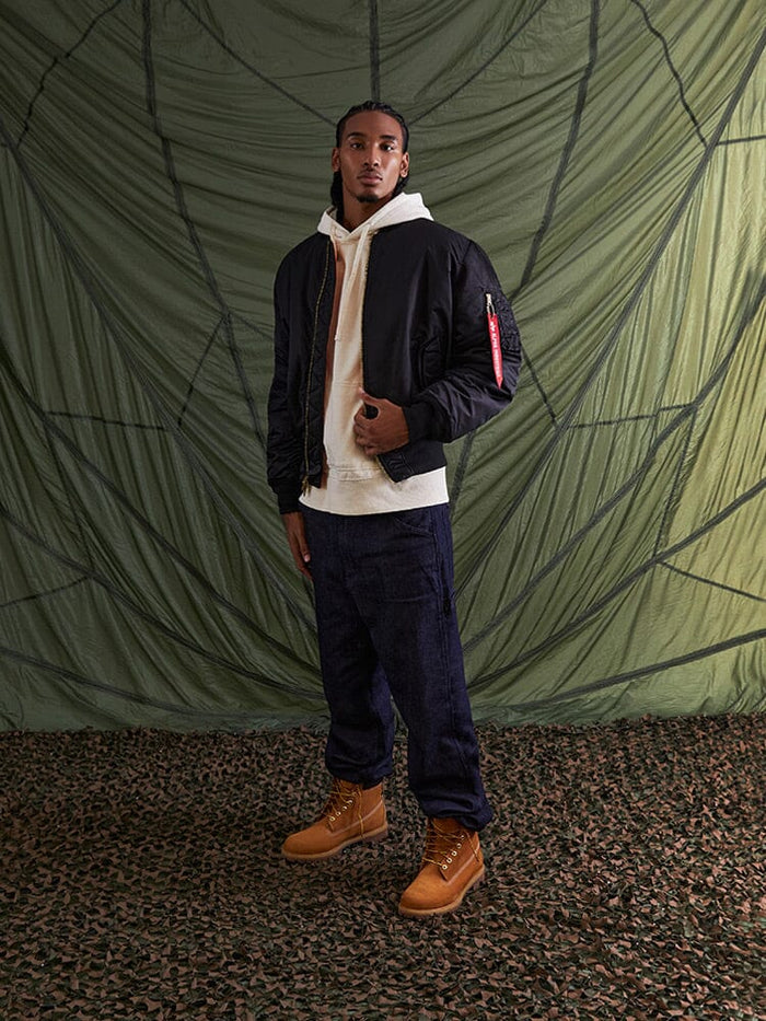 Alpha Industries MA-1 Bomber Jacket in black flight nylon, cream hoodie, dark cargo pants, tan boots.