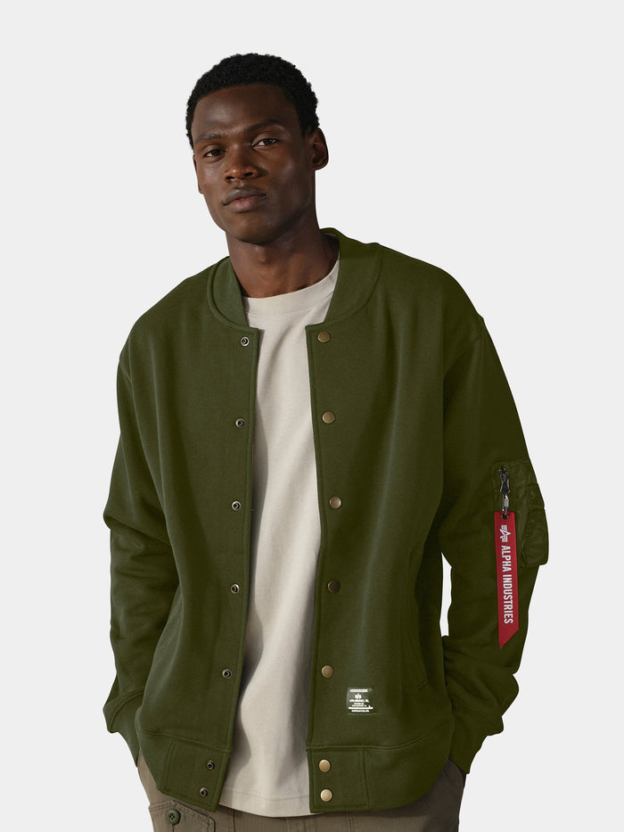 Olive green Alpha Industries MA-1 Fleece Jacket over light gray t-shirt with red sleeve tag.