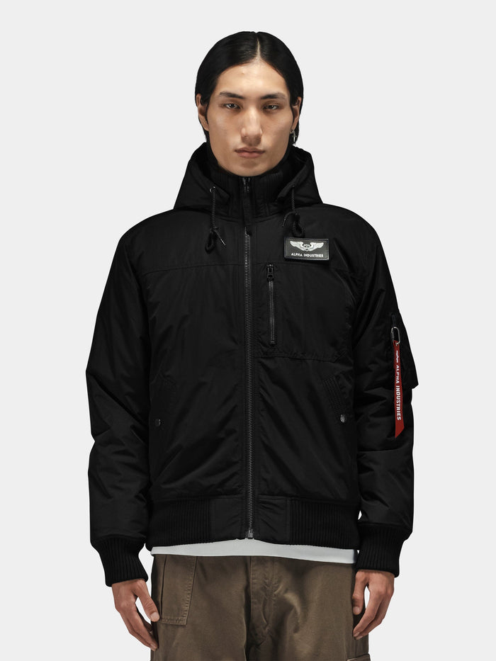 Alpha Industries Hooded Rib Flight Jacket in black with chest patch and utility sleeve pocket, paired with brown pants.