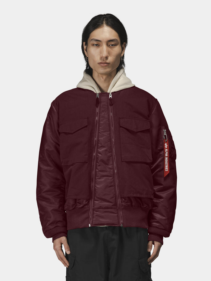 Alpha Industries MA-1 Mixed Cotton Flight Jacket in burgundy with front pockets, beige hooded sweatshirt, and black pants.