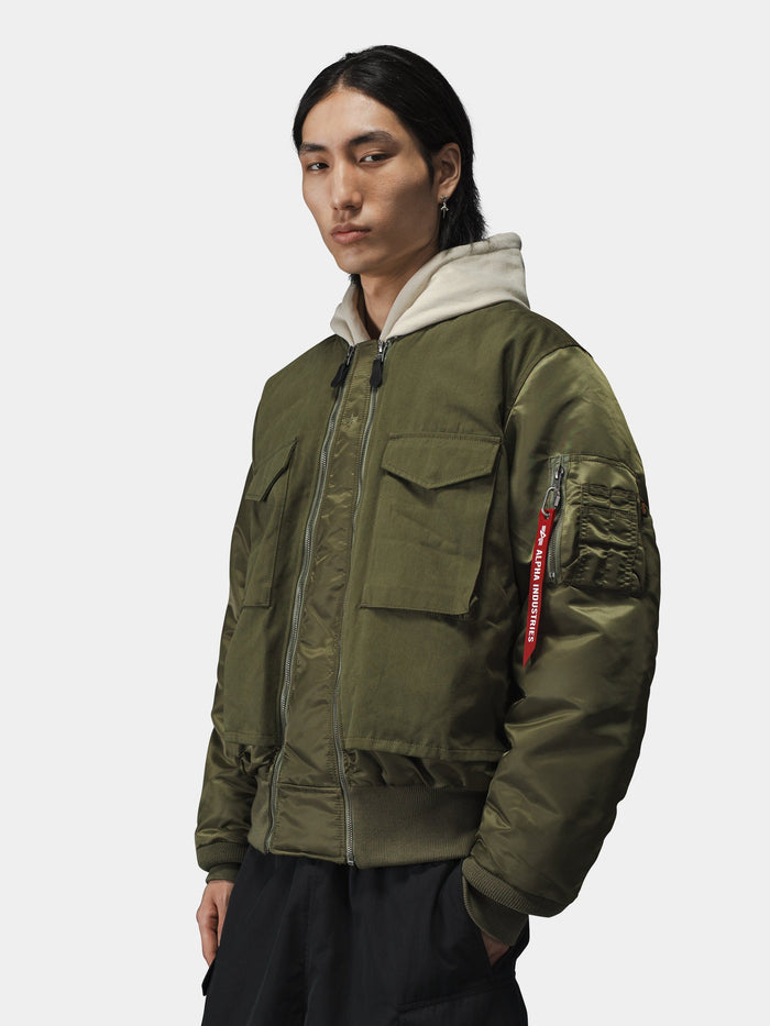 Alpha Industries MA-1 Mixed Cotton Flight Jacket in olive green, layered over a beige hoodie.