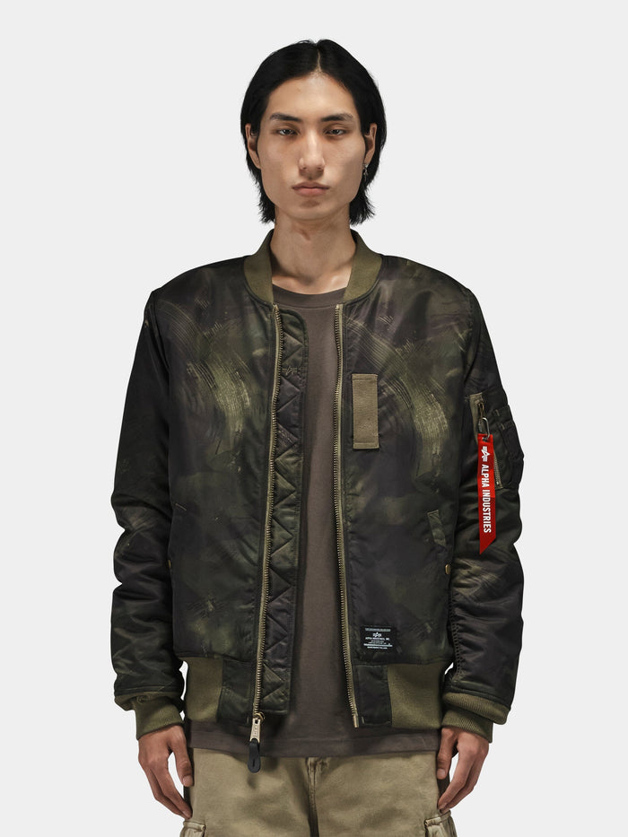 Alpha Industries MA-1 Mod Bomber Jacket in dark green camo with red Remove Before Flight tag and utility pocket.