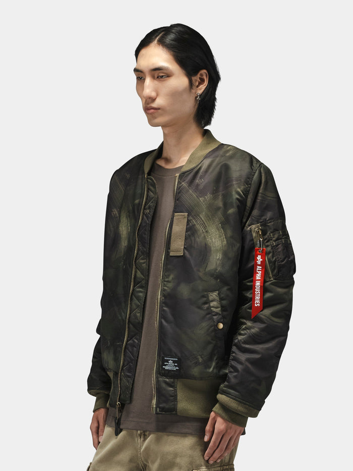 Alpha Industries MA-1 Mod Bomber Jacket in green camo with red Remove Before Flight tag and utility pocket.