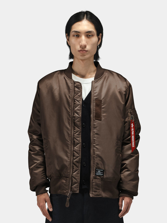 Alpha Industries MA-1 Mod Bomber Jacket in brown with ribbed cuffs and waistband, zip closure, over black cardigan and white shirt.
