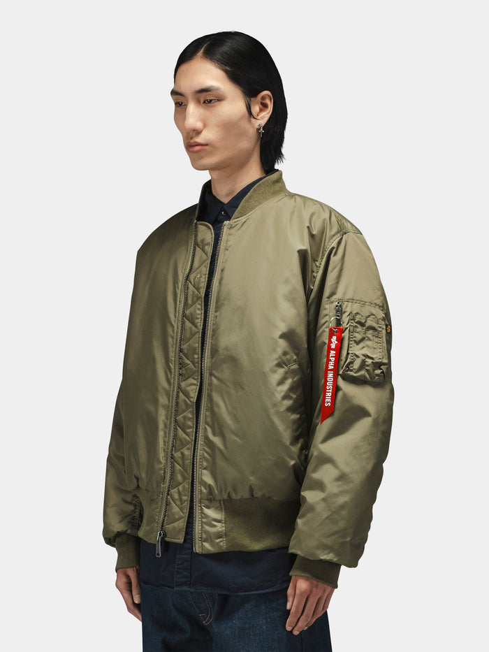 Alpha Industries MA-1 Oxford Flight Jacket in olive green with zip pocket and red "Remove Before Flight" tag on the sleeve.