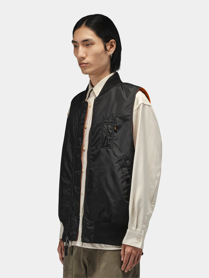 Alpha Industries MA-1 Oxford Vest in black, featuring button-up front, layered over a cream shirt and khaki pants.