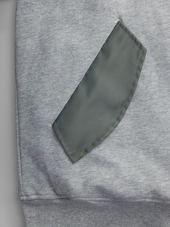 A close-up of MA-1 Zip Up Hoodie in gray by Alpha Industries, showcasing a green pocket detail sewn onto it.