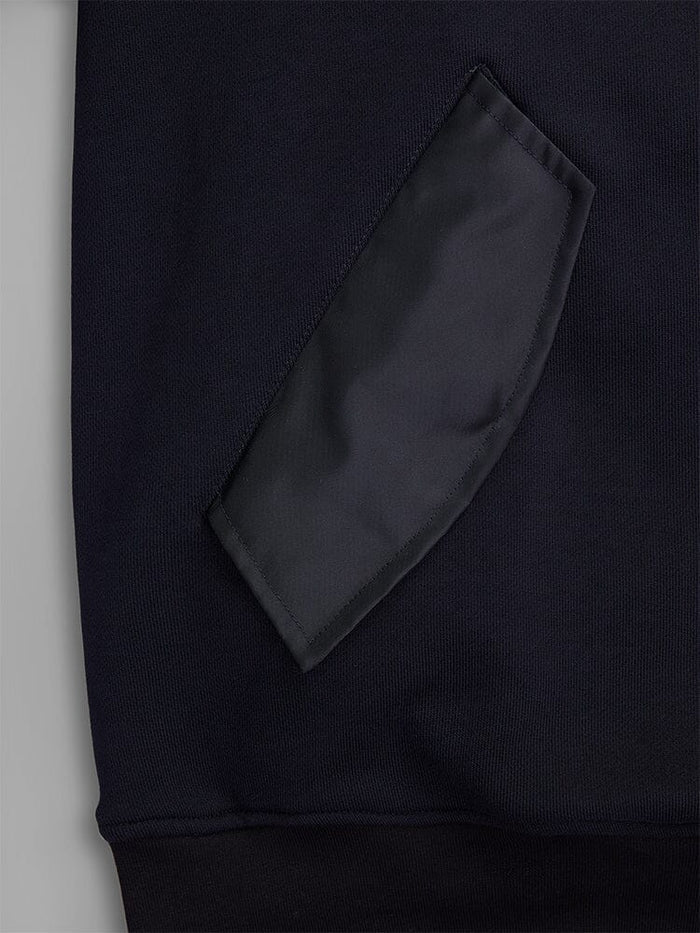 Close-up of a fabric patch pocket on the MA-1 Zip Up Hoodie by Alpha Industries. The pocket is crafted from black French terry fabric, showcasing its texture and stitching details on this dark garment.