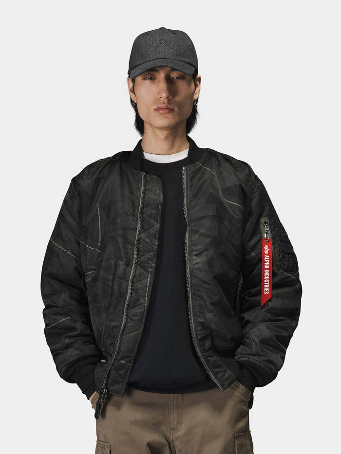 Alpha Industries MA-1 Zippered Print Flight Jacket with red tag, black shirt, khaki pants, grey baseball cap.