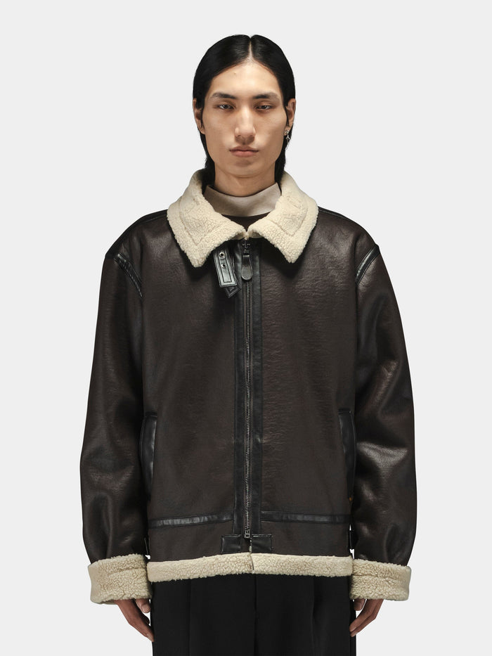 Alpha Industries Mouton B-3 aviator jacket in dark brown with light beige collar and cuffs, layered over a high-neck top.