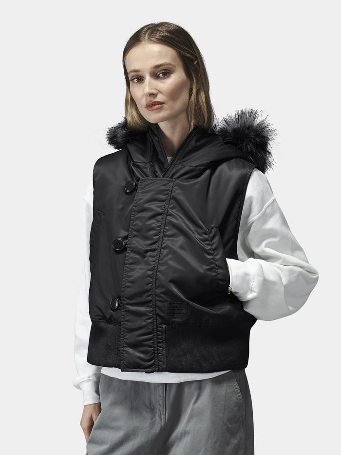 Alpha Industries N-2b Vest Womens in black with faux fur hood. Worn over a white long-sleeve shirt and gray pants.