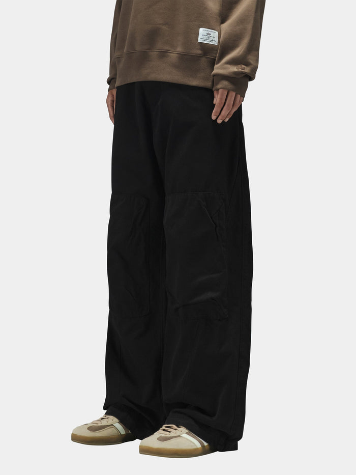 Alpha Industries Oversized Washed Pant, black cargo style with large knee patches. Brown sweatshirt and beige sneakers.